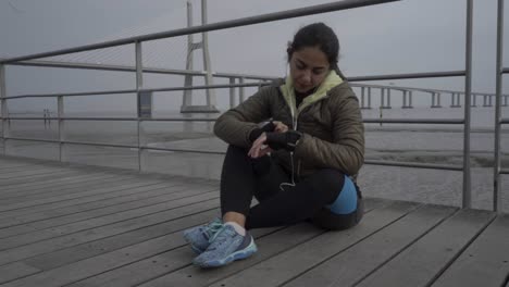 Beautiful-hindu-woman-wearing-port-clothing-sitting-on-wooden-pier-and-preparing-to-workout